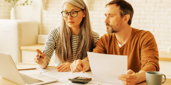 Mature middle-aged couple family wife and husband counting funds, savings declarations, investments,paperwork, financial documents, bankruptcy, court case, bills, pension with laptop.